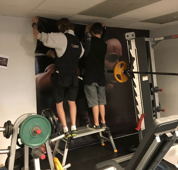 To menn monterer veggdekor på treningssenter